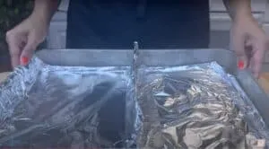 Hands holding a baking sheet lined with aluminum foil, ready for cooking.